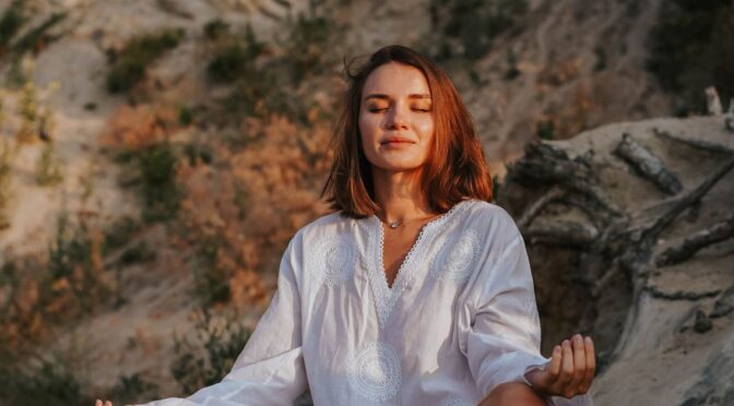 Mulher meditando ao ar livre, representando equilíbrio e bem-estar