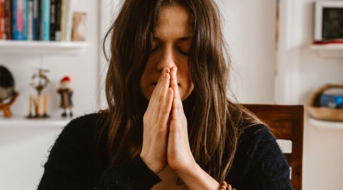 Mulher com as palmas unidas meditando, representando calma e autocuidado