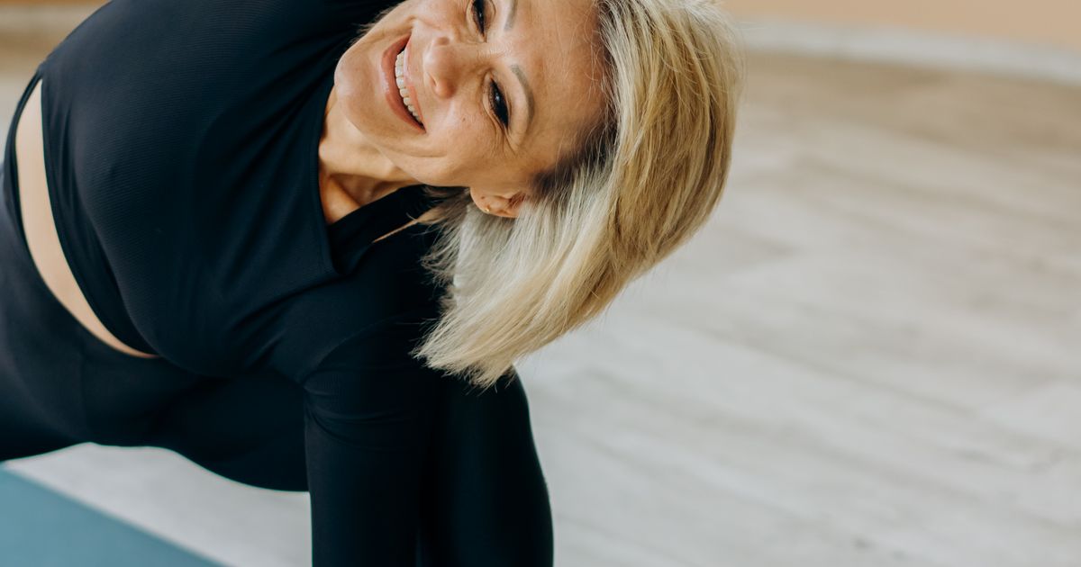 Mulher madura praticando yoga em casa, representando bem-estar e autoestima